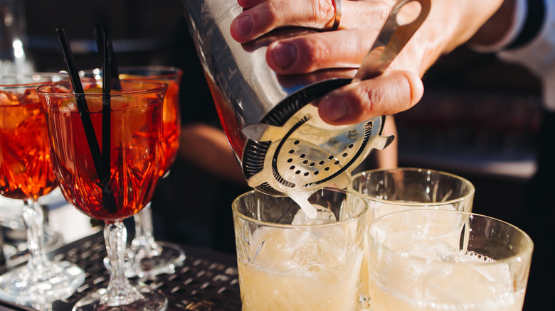 A bartender pours drinks from a cocktail shaker into rocks glasses