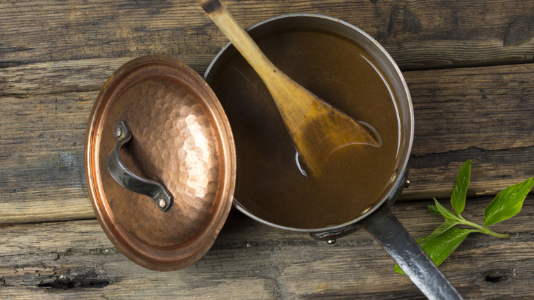 Gravy in a copper sauce pan with wood spoon on wood table.