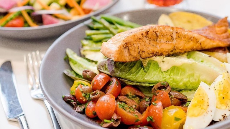 salmon filet on top of dressed whole romaine lettuce leaves with tomato and Kalamata olive salad, hard boiled eggs wedges, and green beans from The Pioneer Woman Mercantile