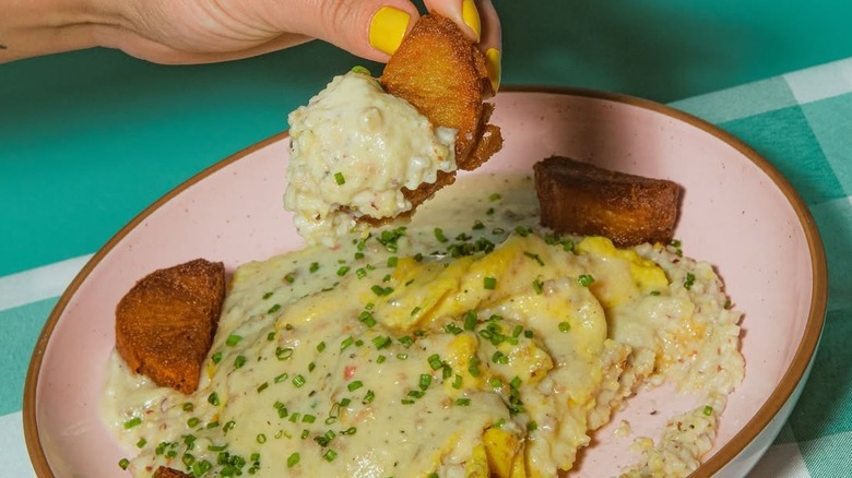 Hands eating from a plate of shrimp and grits at Millers All Day