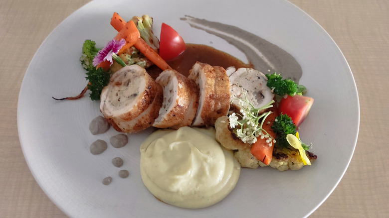 A chicken ballotine on a plate with vegetables and garnishes.