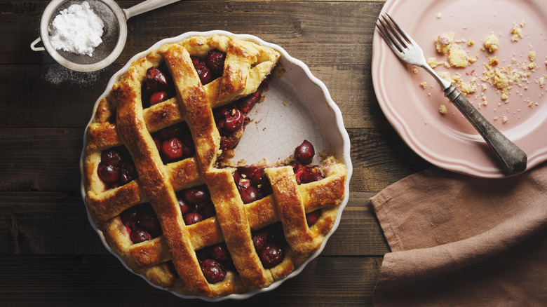 A lovely cherry pie beside a plate topped with crumbs from a finished piece.