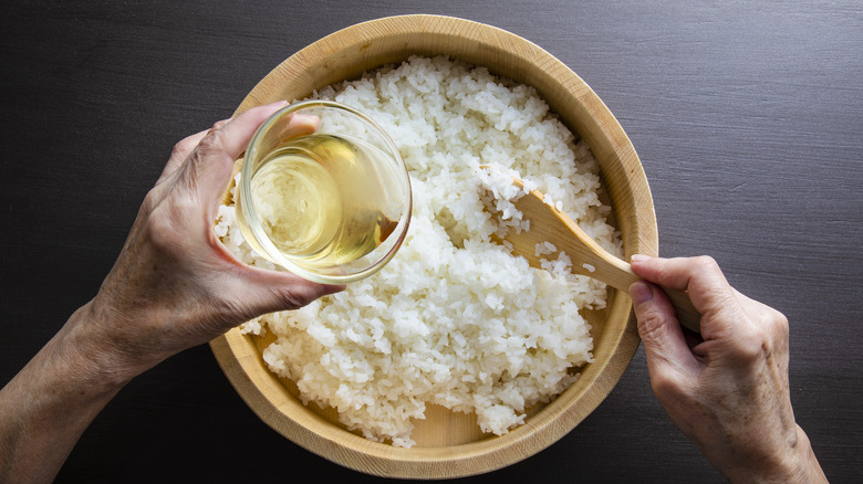 person adding vinegar mixture to sushi rice