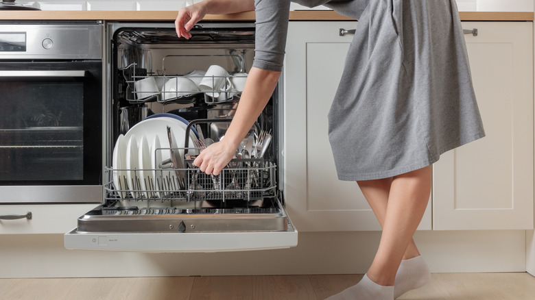 Woman in a gray dress loading a dishwasher