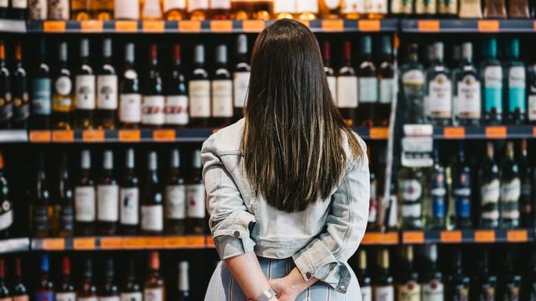 A person peruses bottles of alcohol on store shelves.
