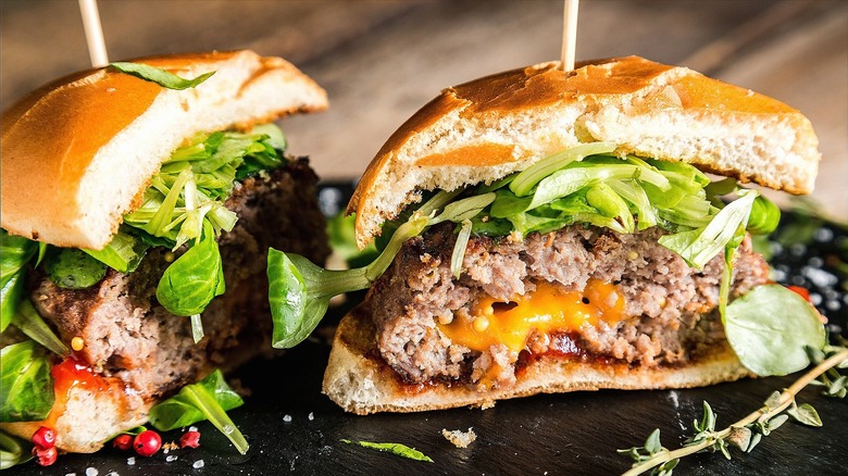 Halved Juicy Lucy burger with melted cheddar cheese and fresh greens on a black serving board