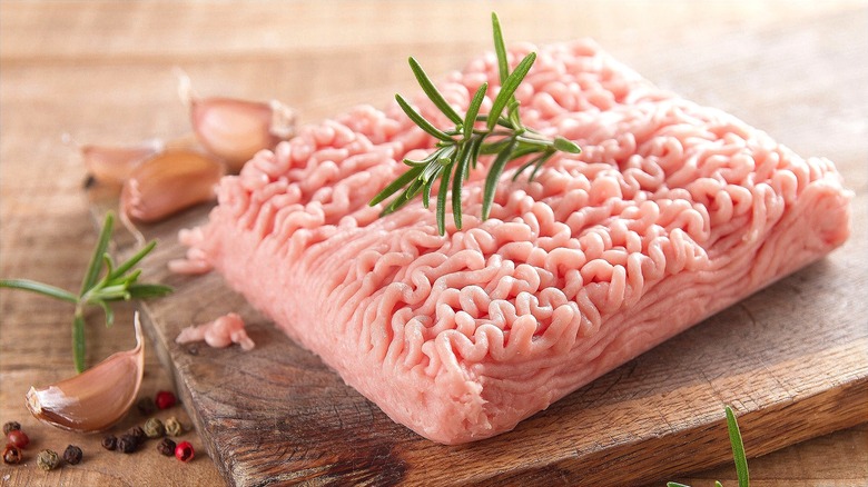 Pound of raw ground turkey with a sprig of fresh rosemary on a wooden board