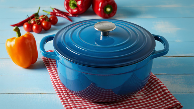 A vibrant blue enameled cast iron Dutch oven sits on a red and white checkered cloth
