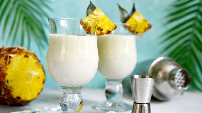 2 pina coladas next to a sliced pineapple.