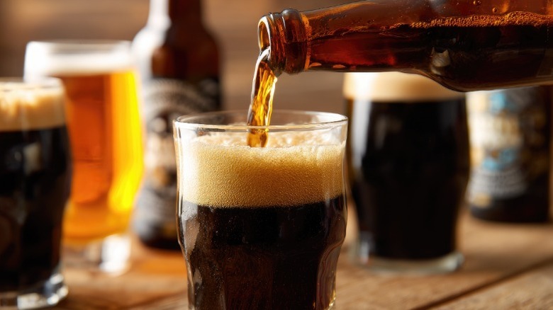 A dark beer being poured from a bottle into a glass with different beer styles sitting in glasses behind it.