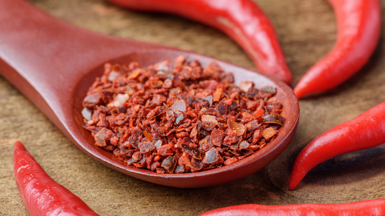 Chili flakes on a wooden spoon surrounded by chili peppers