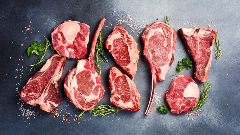An array of steaks laid on a counter with salt and herbs