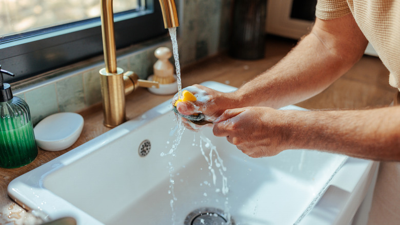 Man washing dishes in a single-basin kitchen sink.