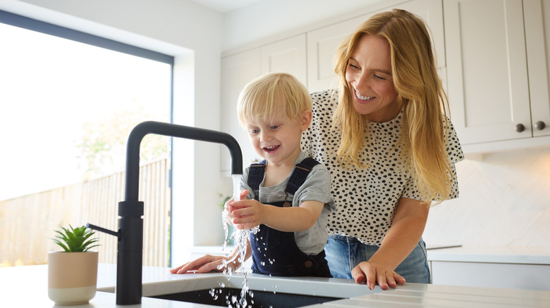 Mother with child washing hands in single-basin kitchen sink.