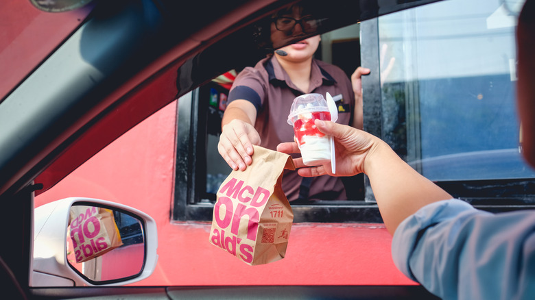 A person takes a bagged McDonald's order from an employee at a drive-through.