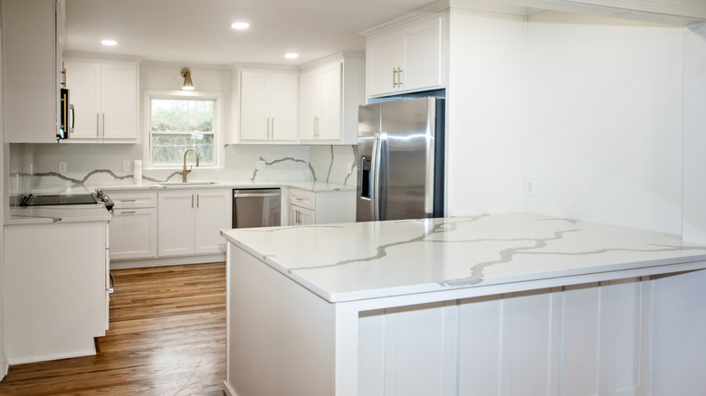 Remodeled kitchen stands empty with white and gray quartz countertop and backsplash