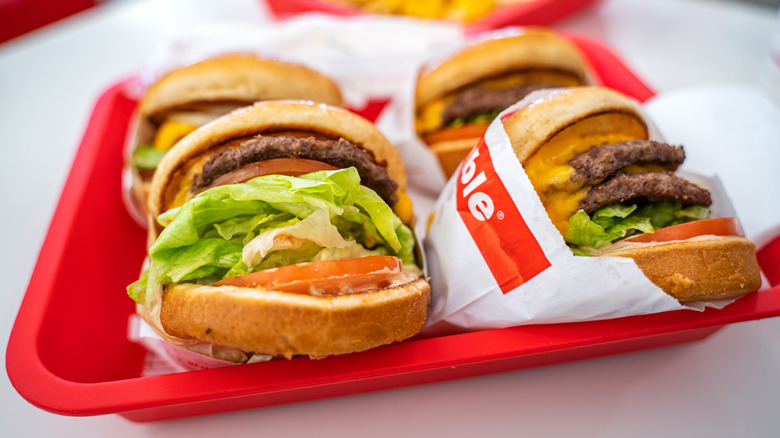 Four In-N-Out burgers with lettuce, tomato, cheese, and patties bursting out of the buns.