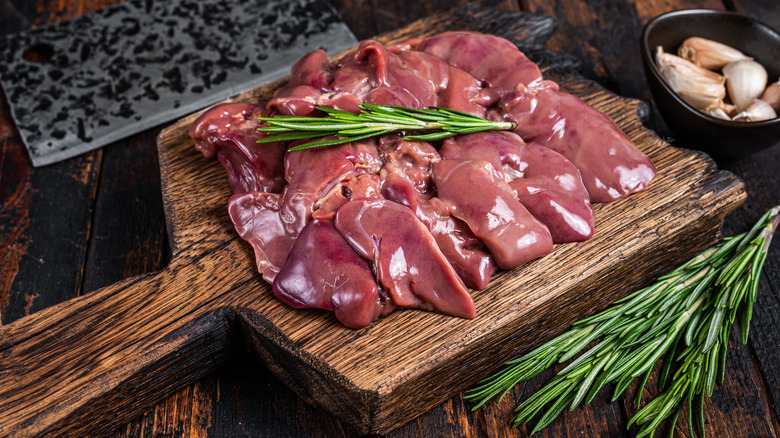 A cutting board with raw livers and a rosemary garnish