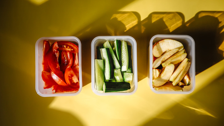 Three Tupperware containers with freshly cut fruits and veggies