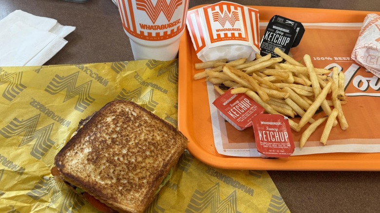 Whataburger with Texas toast instead of buns next to fries, sauces, and a drink