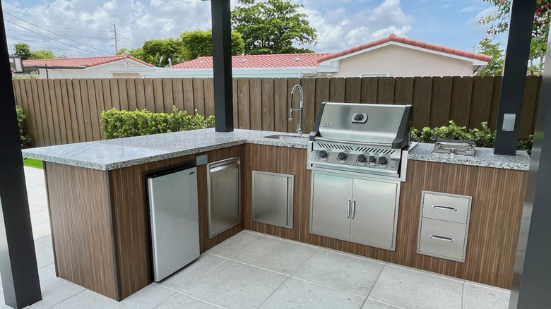 Outdoor bar setup in a backyard with mini-fridge and grill