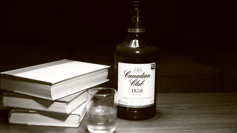Bottle of Canadian Club 1858 Original next to a glass and books.