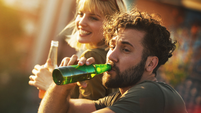 Two people drink beer from bottles outdoors