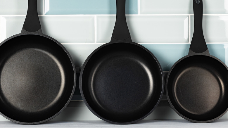 Three cast-iron skillets arranged against a tile wall.