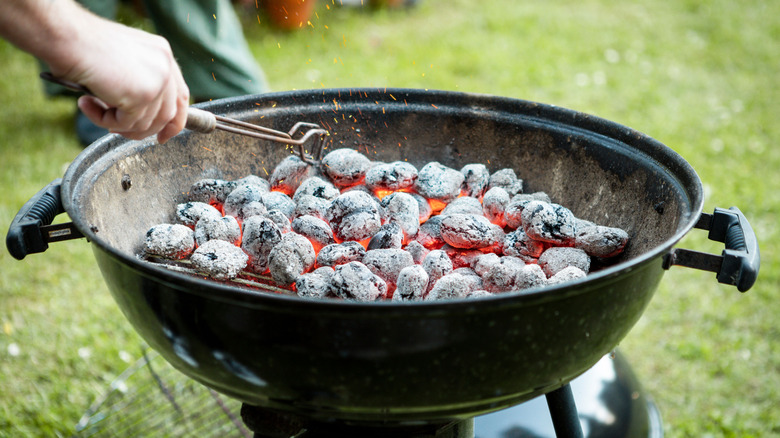 Person using tongs to arrange charcoal briquettes in a charcoal grill