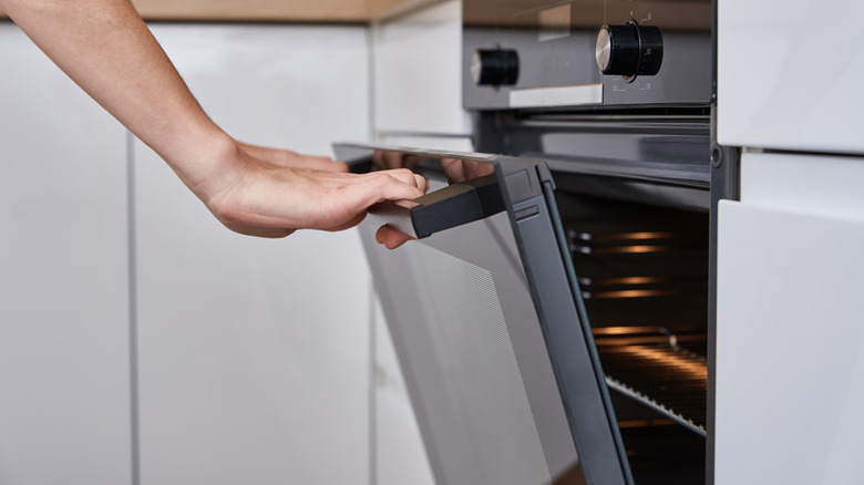 A hand opening an oven door.