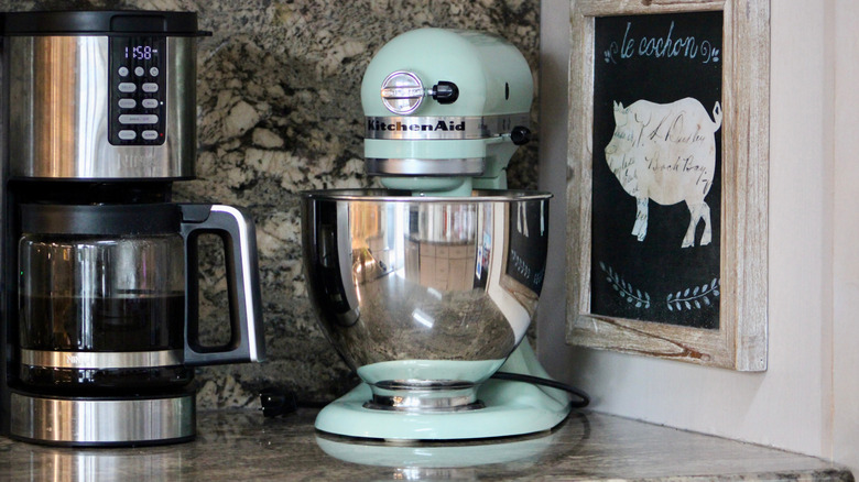 Pale blue KitchenAid stand mixer on a kitchen counter next to a coffee machine and wall art