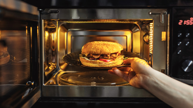 A hand putting a burger on a plate into a microwave