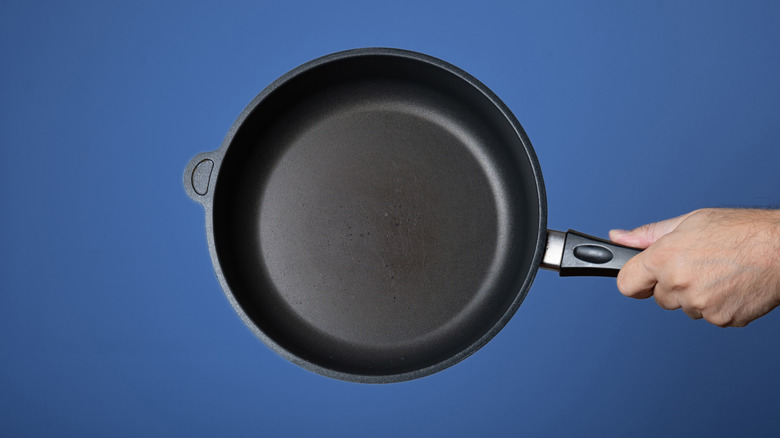 An individual holding a nonstick pan against blue background.