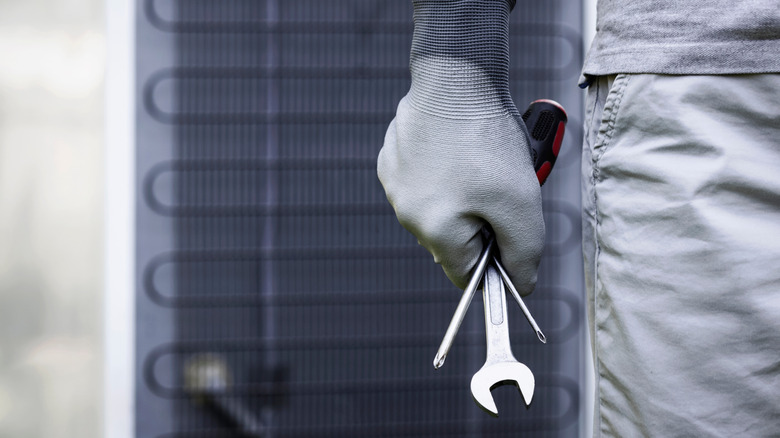 Person with a gloved hand holding a wrench and screwdriver