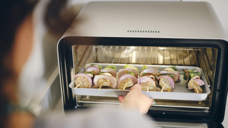 Person taking shrimp and veggie kebabs out of the toaster oven