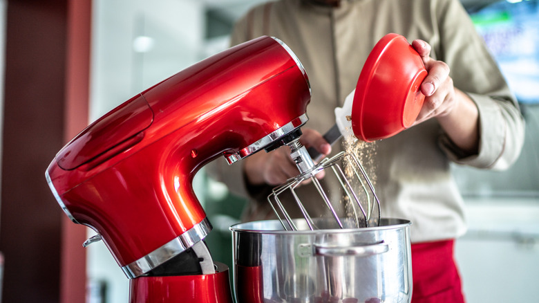 A person pouring ingredients into a red stand mixer