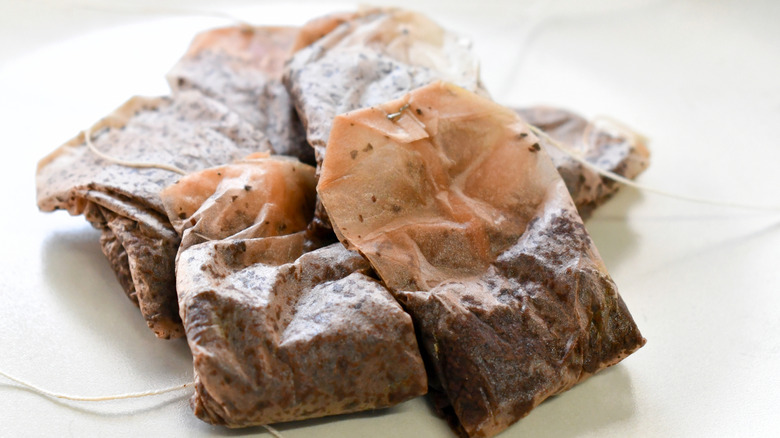 Several used tea bags on a small plate.