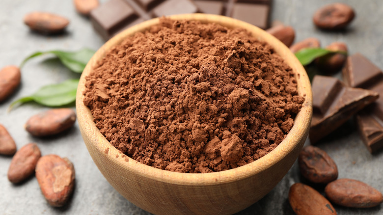 Cocoa powder in a wooden bowl surrounded by cacao beans and chocolate