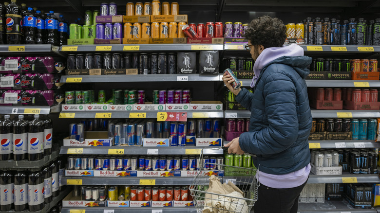 Man inspecting an energy drink can label while holding a grocery basket and shopping for energy drinks
