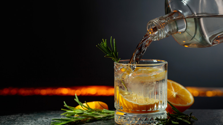 Gin being poured from a bottle into a glass for a gin and tonic cocktail