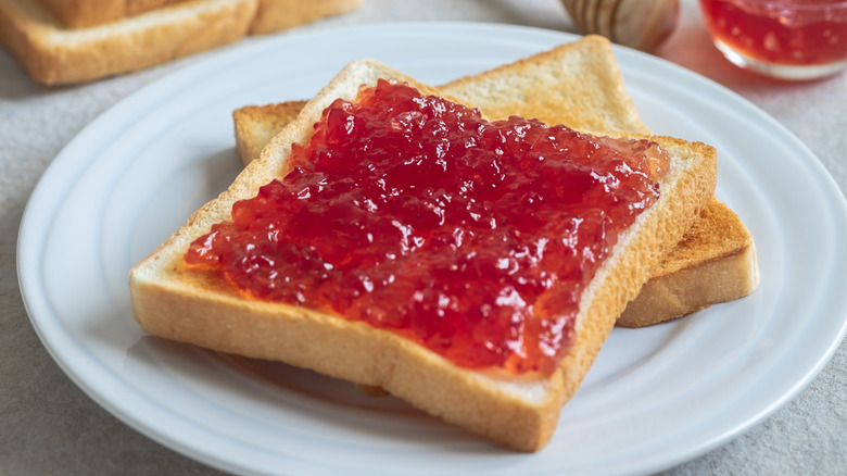 Two pieces of toast on a white plate, top piece of toast is covered with red jam