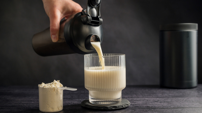 Protein drink. Pouring protein shake in a glass. Dark background.