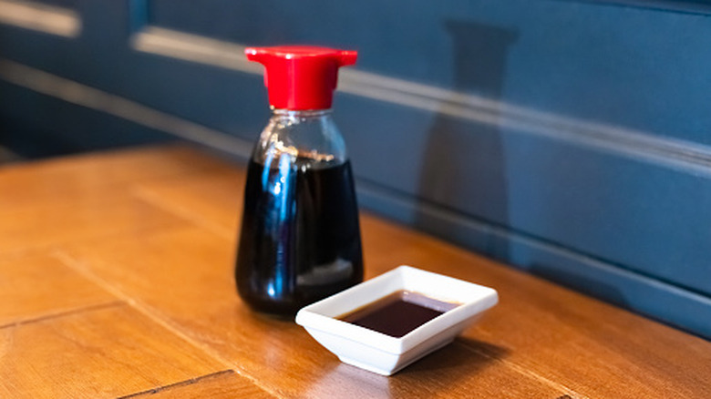 A soy sauce bottle and small dish of soy sauce on a wooden table.