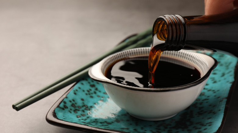 Soy sauce being poured from a bottle into a bowl.
