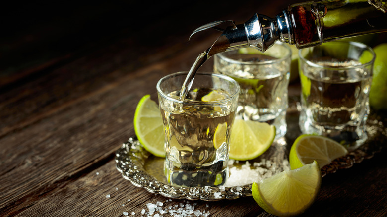Tequila being poured into a shot glass with slices of lime beside it