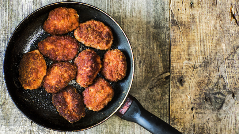 A crowded pan with nine cutlets with a perfectly brown exterior