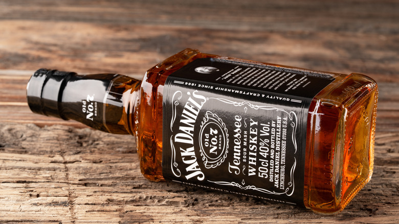 A Jack Daniel's Old No. 7 bottle lying on its side on a wooden surface.