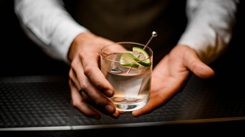 Bartender's hands holding a gin and tonic in a clear glass