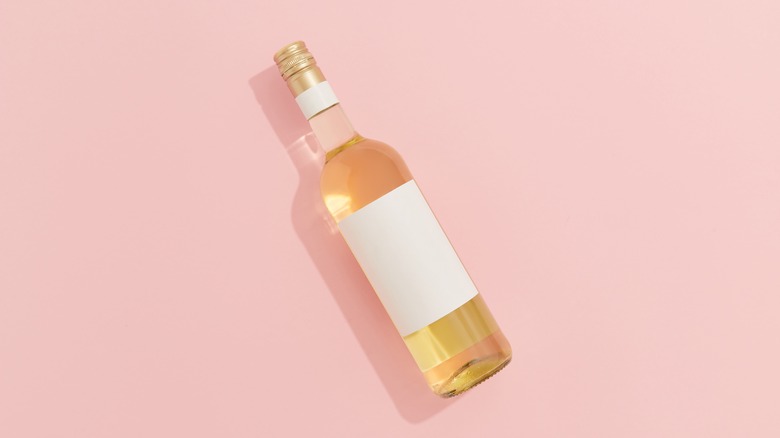 A rosé wine bottle with a blank label over a light pink background