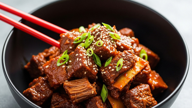 A black bowl with Korean BBQ short ribs and chopsticks
